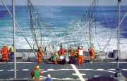 Il ponte poppiero della USS Iowa, con una grande rete parzialmente eretta visibile al centro dell'immagine. Molti uomini in tenuta arancione stanno adoperandosi per liberare un RQ-2 Pioneer bloccato nella rete.
